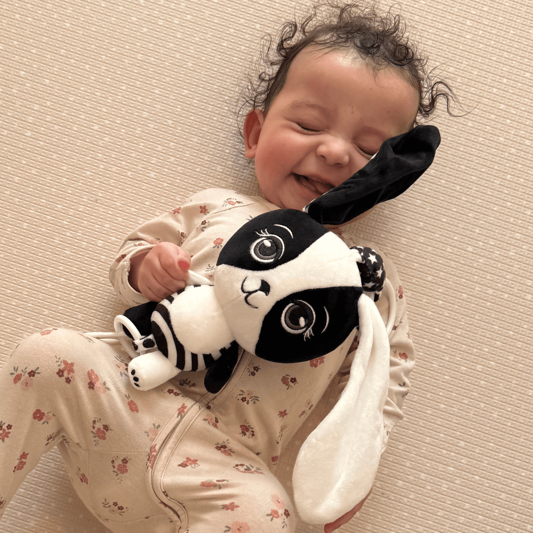 Smiling baby cuddling Billie the Bunny high contrast black and white sensory toy – ideal for newborn bonding and visual development