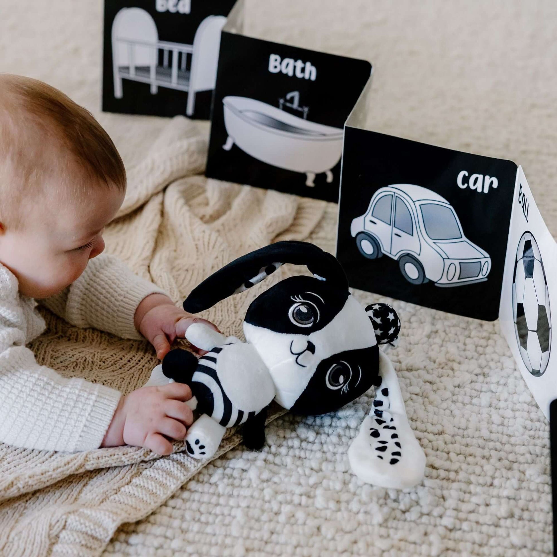 Newborn in tummy time playing with Billie the Bunny toy and high-contrast black and white book from Young Wonderer