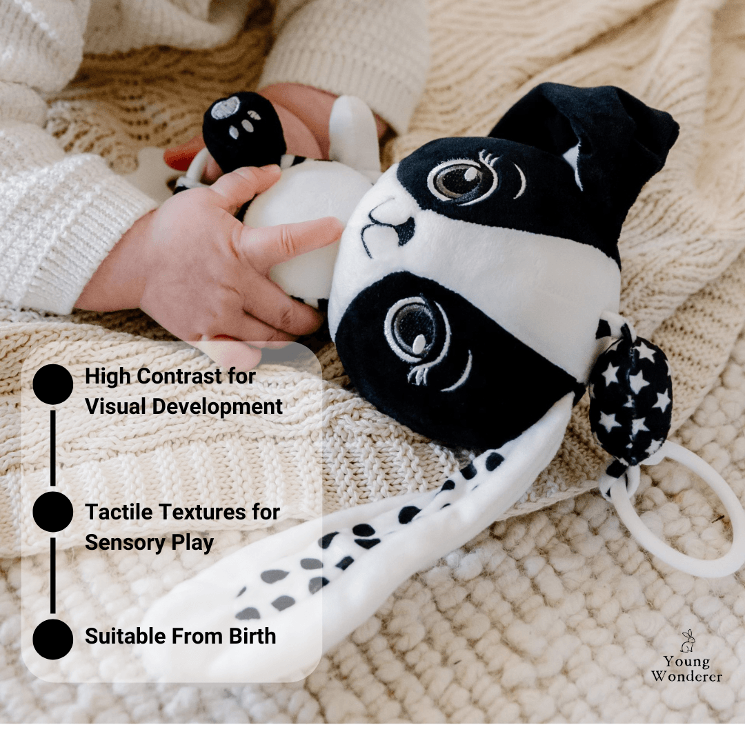 Black and white plush toy held by a child's hand on a soft surface, with text highlighting features.